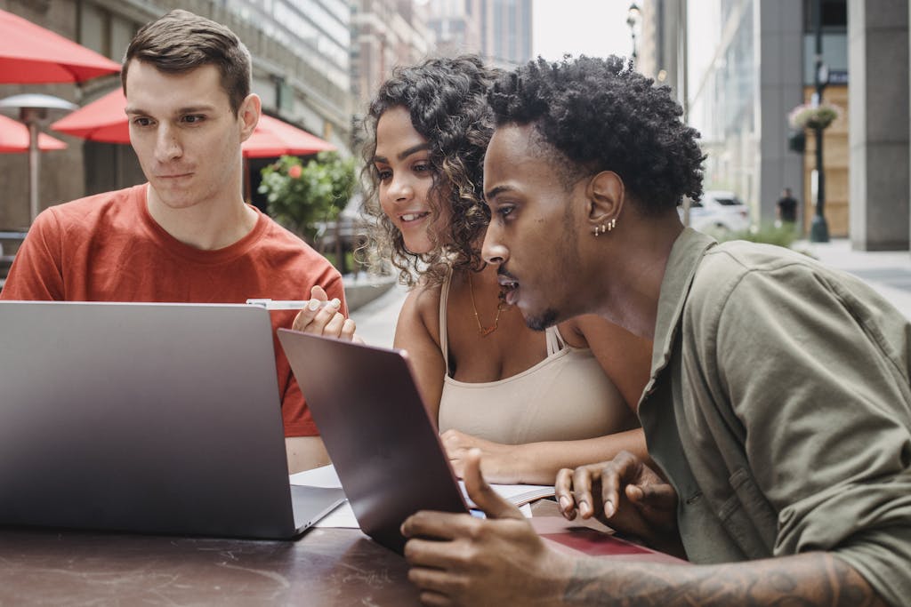 Concentrated young multiracial students sitting in street cafe and using laptops while preparing for exams on sunny day